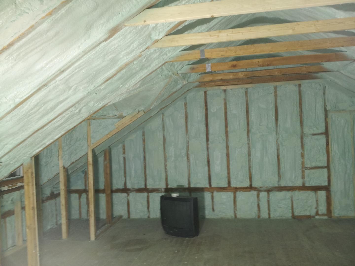 Grenier avec poutres en bois, murs et plafond recouverts d'une isolation en mousse projetée blanche.