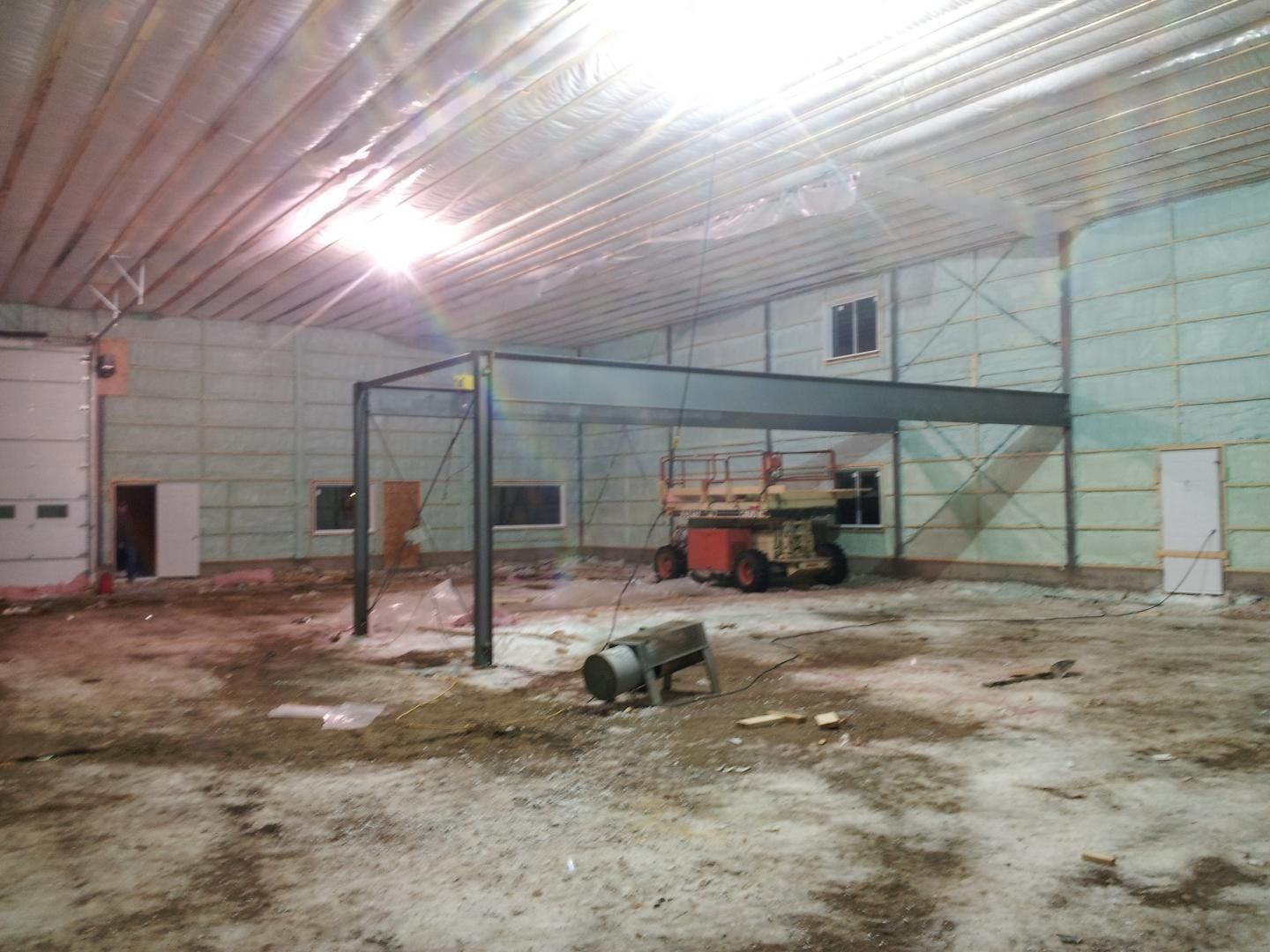 Intérieur d'un grand bâtiment inachevé avec poutres métalliques, isolation et équipement de construction.