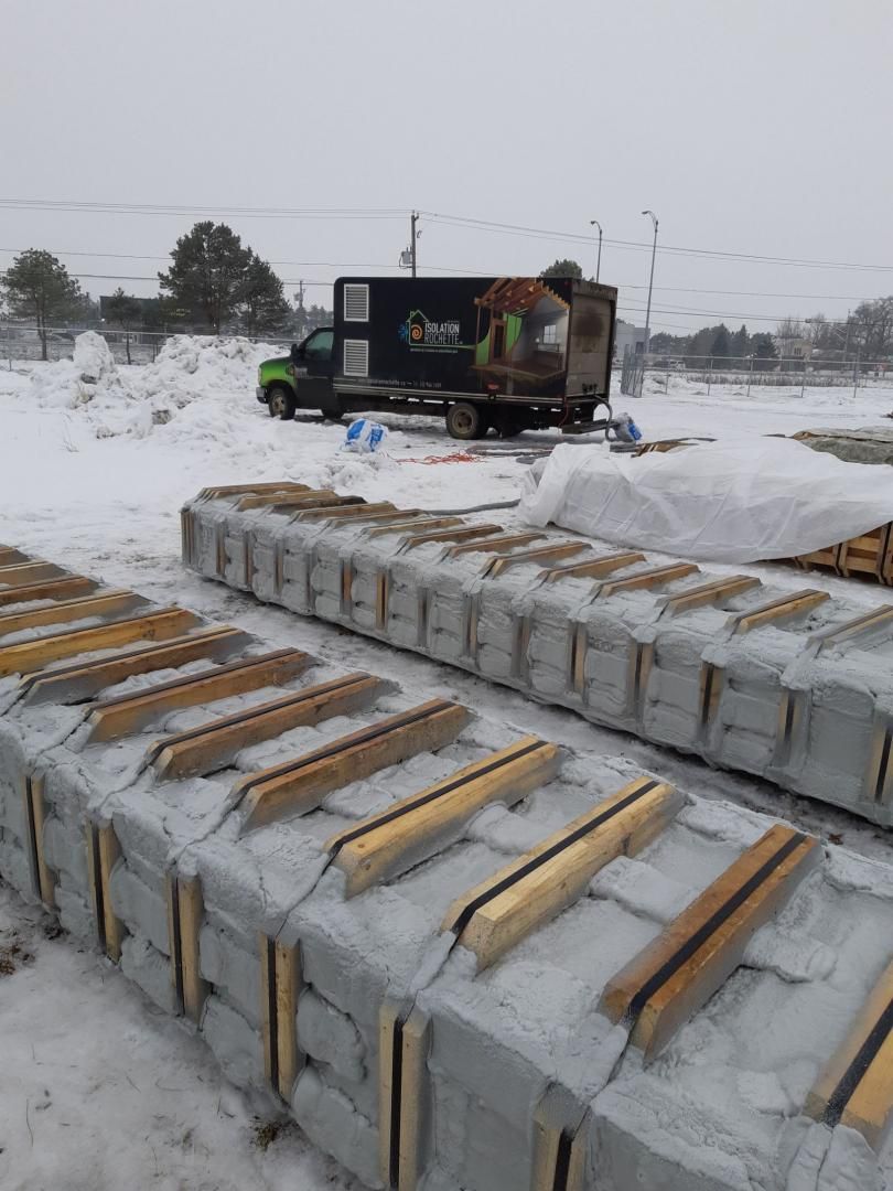 Chantier de construction sous la neige : matériaux empilés, camion avec ouvrier, ciel blanc couvert.