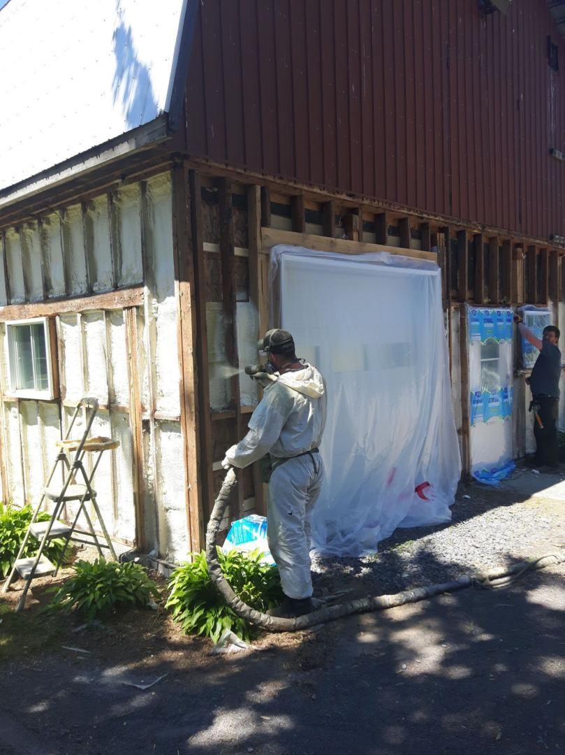 Un homme en combinaison de protection pulvérise de la mousse isolante sur le mur extérieur d'un bâtiment.