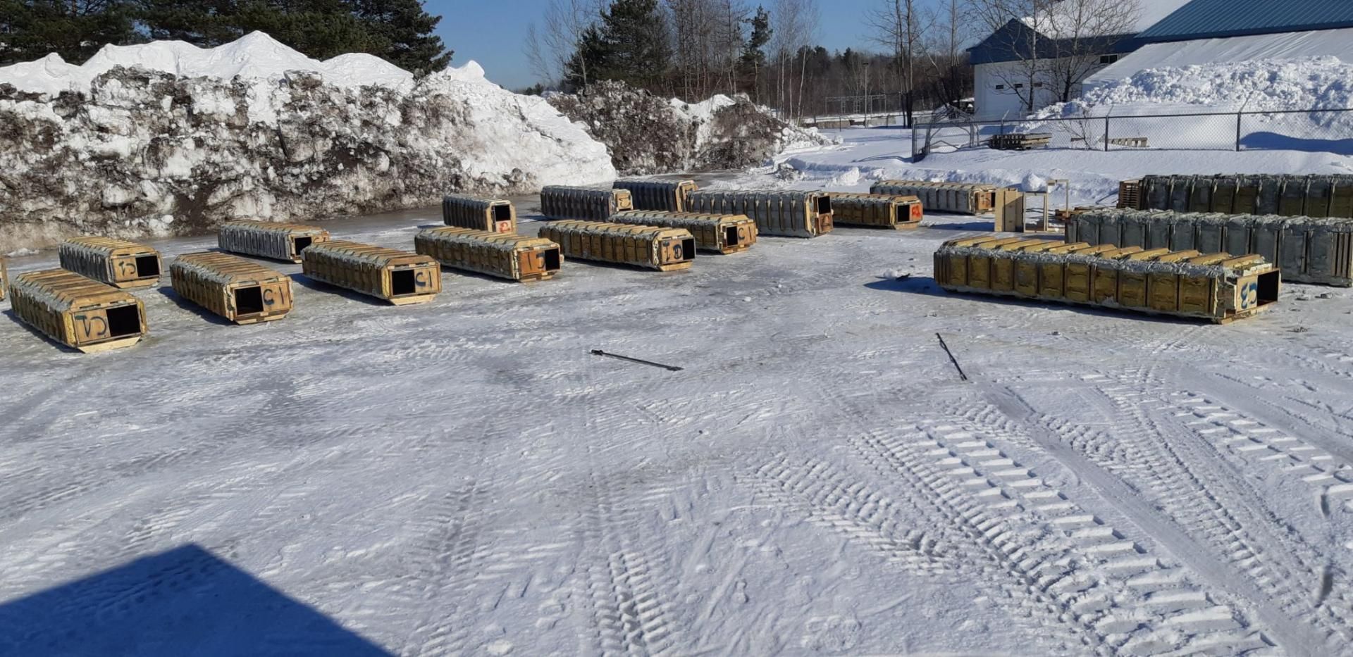 Des structures en bois reposent sur un sol recouvert de neige devant un grand banc de neige.