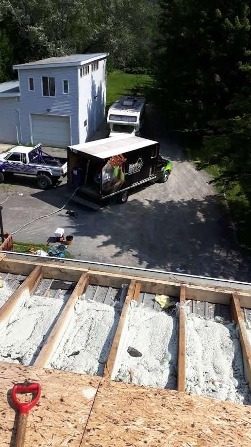 Chantier : Toiture avec planches apparentes et isolation, vue d'une maison et de véhicules dans l'allée.