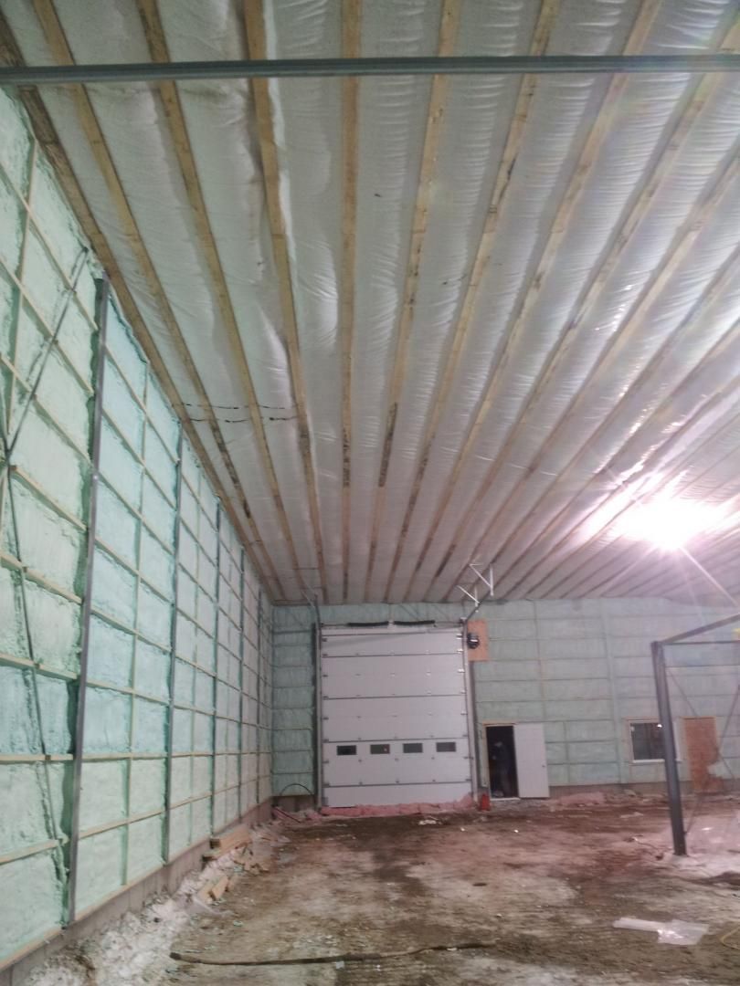 Intérieur d'un bâtiment aux murs et au plafond isolés. On aperçoit une porte de garage fermée et un sol en béton.