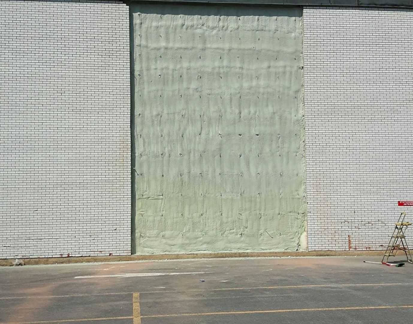 Section de mur en béton avec différents panneaux texturés et un parking stationné.