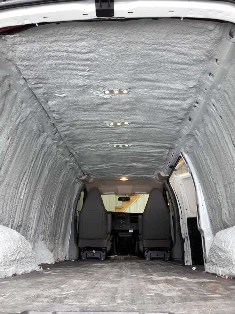 Intérieur du fourgon isolé avec de la mousse projetée grise; sièges visibles à l'avant.