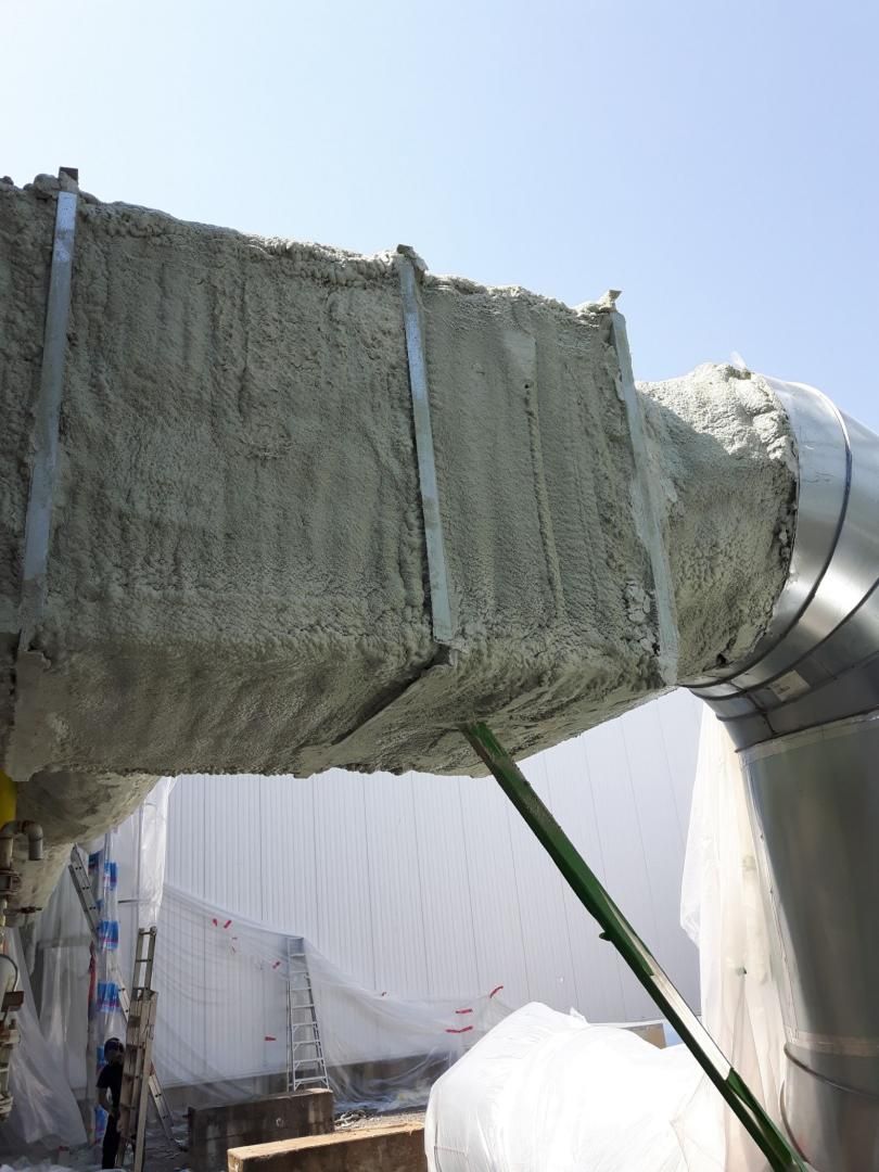 Conduits isolés à l'extérieur, soutenus par un poteau vert. Isolation grise recouvrant le conduit rectangulaire, raccord de tuyau argenté.