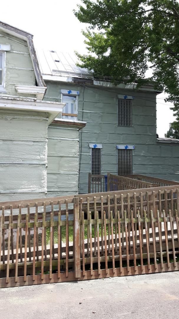 Maison en bois avec peinture vert clair, derrière une clôture en bois.
