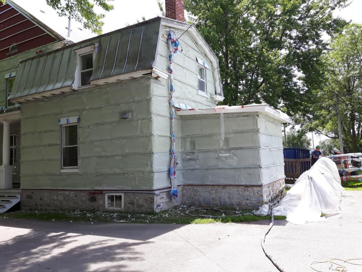 Maison verte claire avec fondation en pierre, toiture en métal et lucarnes; vue extérieure.