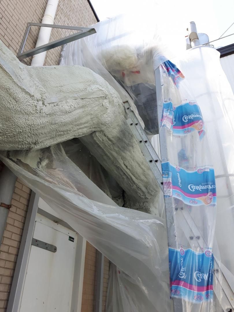 Chantier de construction avec isolation, bâches en plastique et bouteilles d'eau empilées contre un bâtiment.