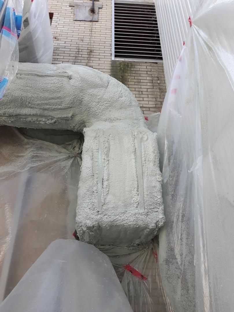 Un tuyau recouvert de gris et enveloppé de plastique, près d'un mur de briques avec un évent.