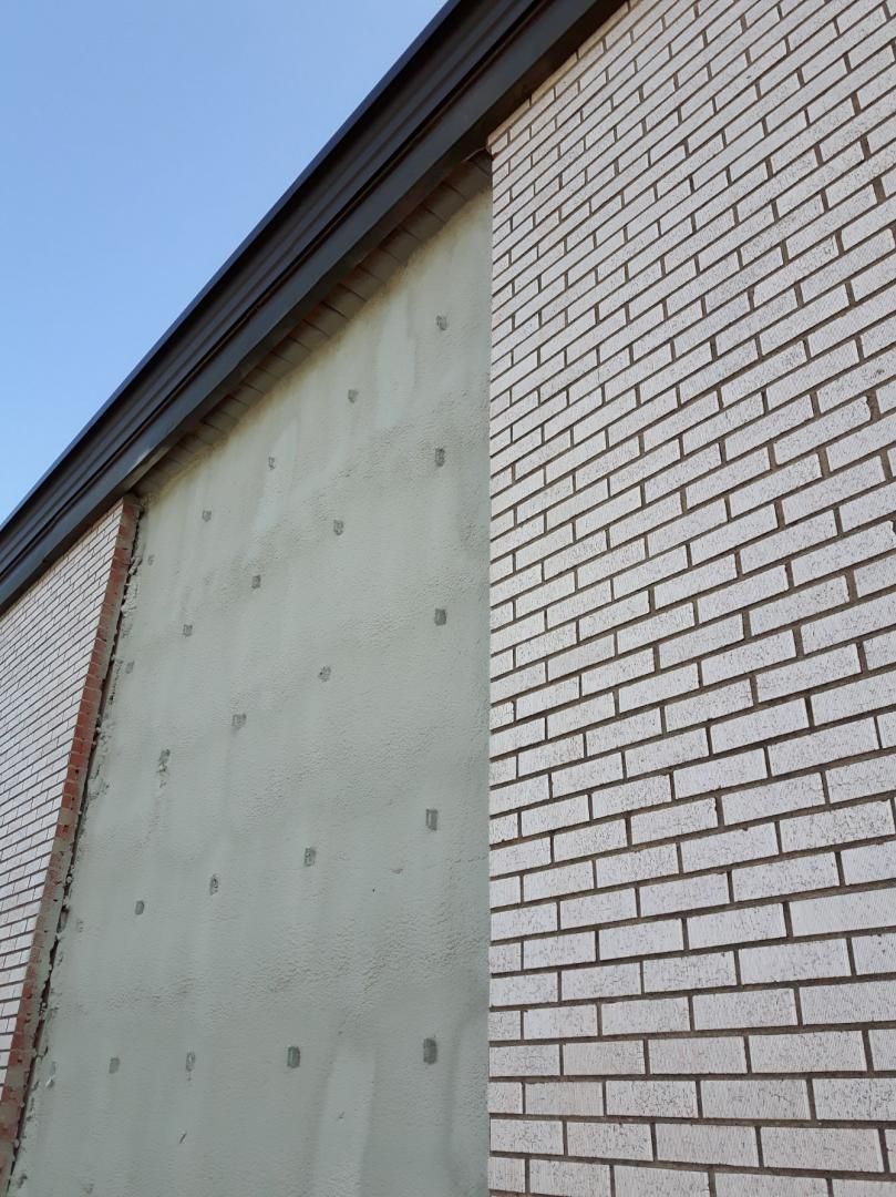 Extérieur d'un bâtiment en briques avec une section en stuc vert clair entre deux murs en briques sous un toit sombre.