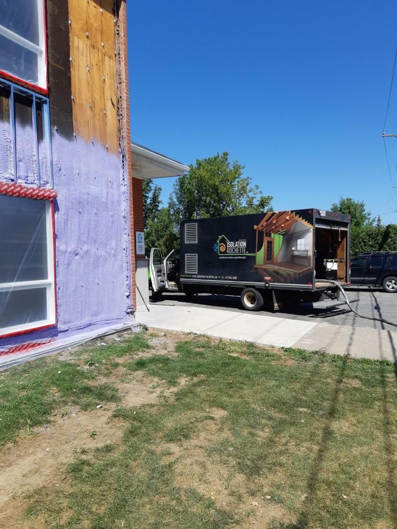 Camion noir garé près d'un bâtiment aux boiseries apparentes. Journée ensoleillée, herbe au premier plan.