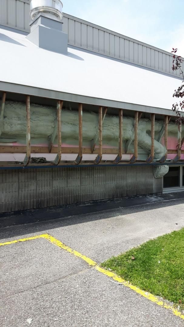 Mur extérieur d'un bâtiment en construction. Ossature bois apparente avec isolation visible. Socle en béton et ligne peinte en jaune.