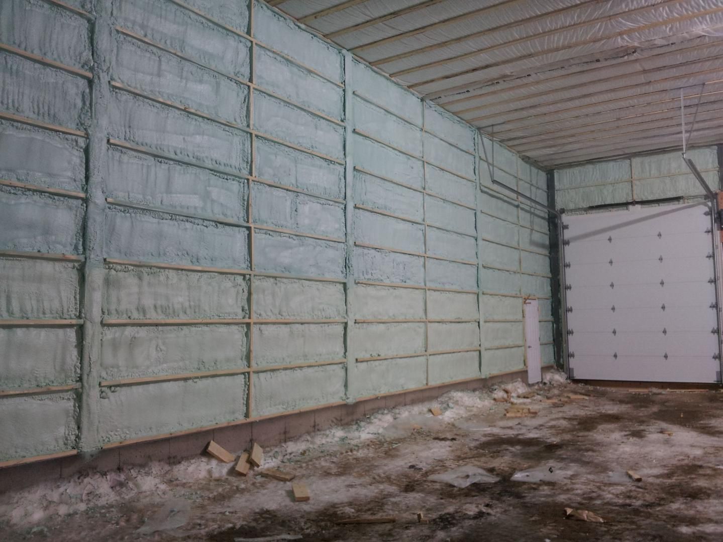 Intérieur d'un garage aux murs isolés par de la mousse vert pâle. On y voit une porte blanche fermée.