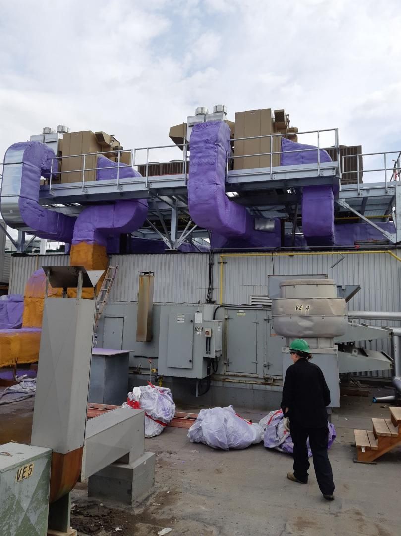 Une personne portant un casque vert à proximité d'un équipement industriel avec une isolation violette, des boîtes et des sacs.