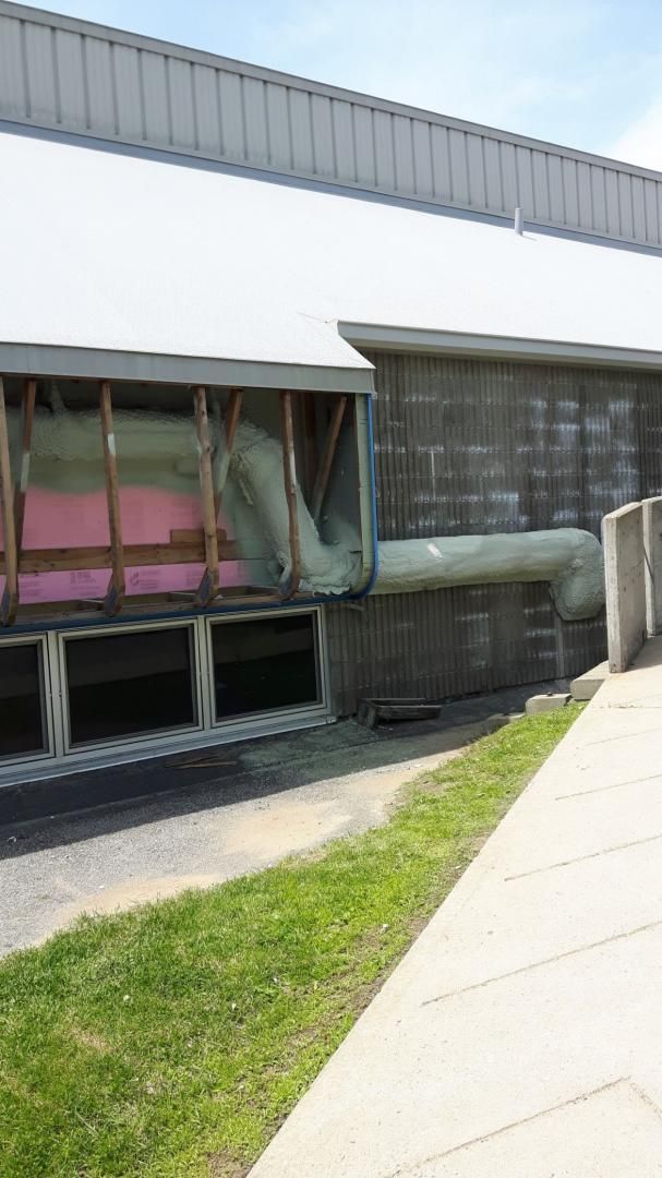 Extérieur du bâtiment avec isolation apparente, poutres en bois et chemin en herbe et en béton.