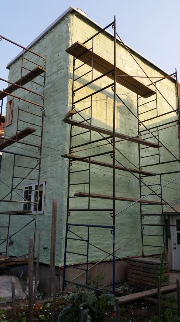 Extérieur du bâtiment en cours de rénovation, recouvert d'une isolation verte avec échafaudage.