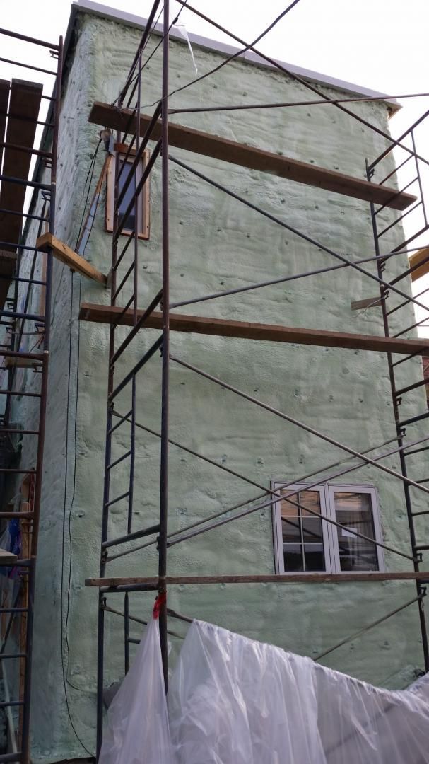 Extérieur du bâtiment avec échafaudage, murs enduits de vert, deux fenêtres.