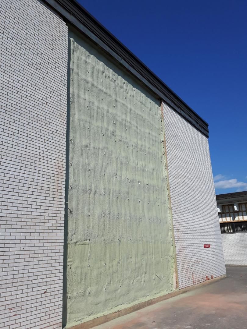 Extérieur du bâtiment avec briques blanches texturées et panneau isolant apparent. Ciel bleu en arrière-plan.