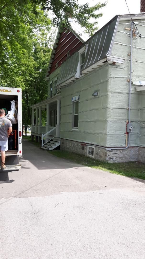 Côté d'une maison vert clair avec un camion de déménagement. Une personne se tient près du camion sur une allée pavée.