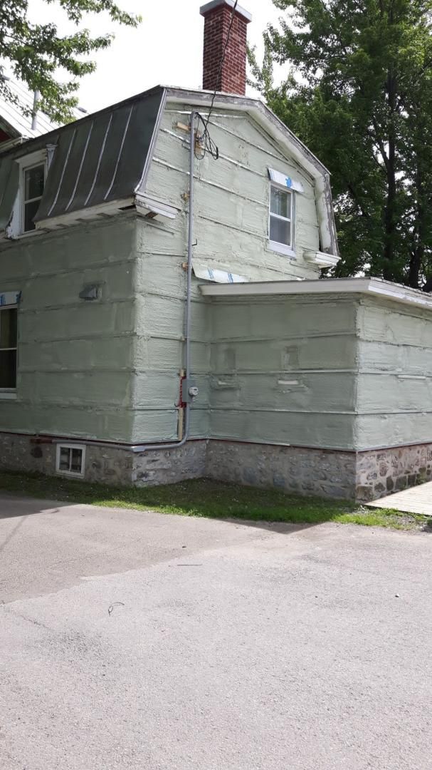 Maison à deux étages peinte en vert avec usure visible, cheminée et une partie inférieure attenante, posée sur une fondation en pierre.