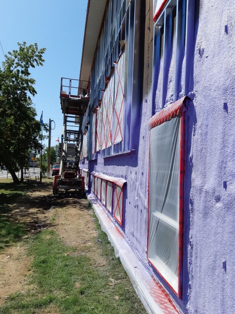 Un bâtiment violet est en travaux grâce à un ascenseur. Les fenêtres sont encadrées de rouge et des affiches sont visibles.