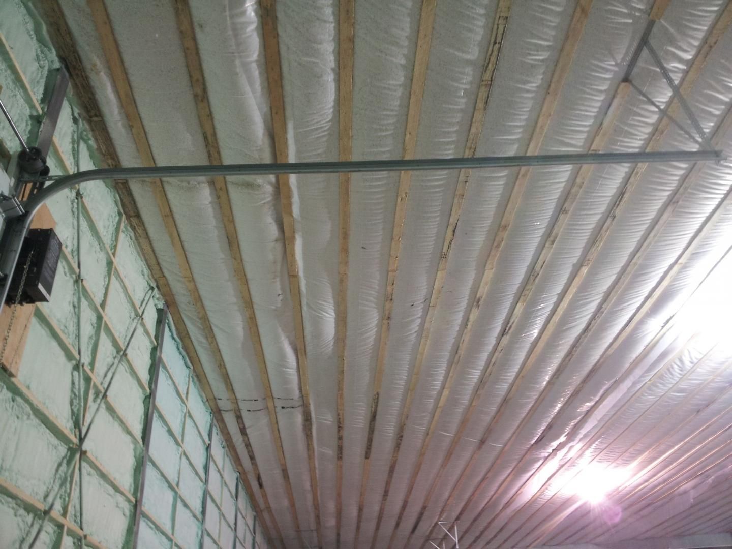 À l'intérieur d'un bâtiment : chevrons de toit avec isolation blanche, tuyau métallique horizontal et boîtier de commande sur le mur.