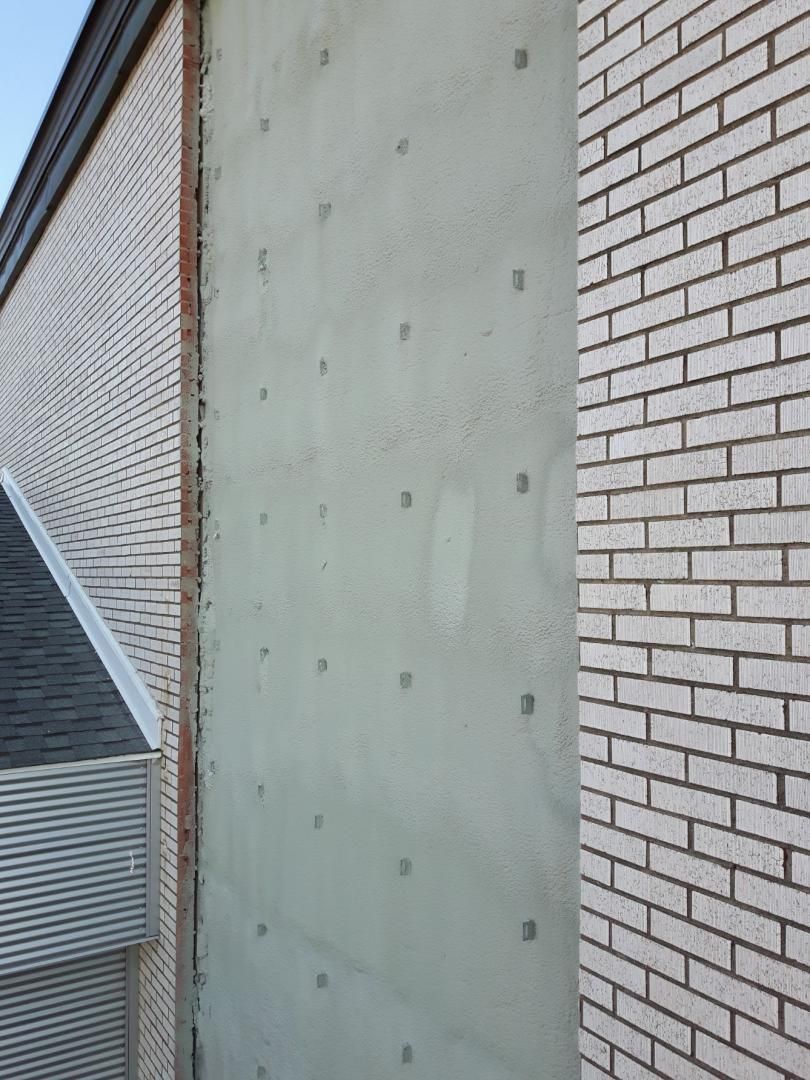 Mur de béton gris avec des carrés sombres régulièrement espacés entre un mur de briques et le bord d'un bâtiment avec un toit en bardeaux.