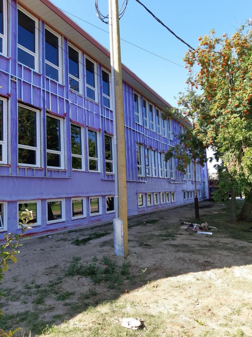 Bâtiment violet avec de nombreuses fenêtres, un poteau électrique devant et des arbres sur la droite.