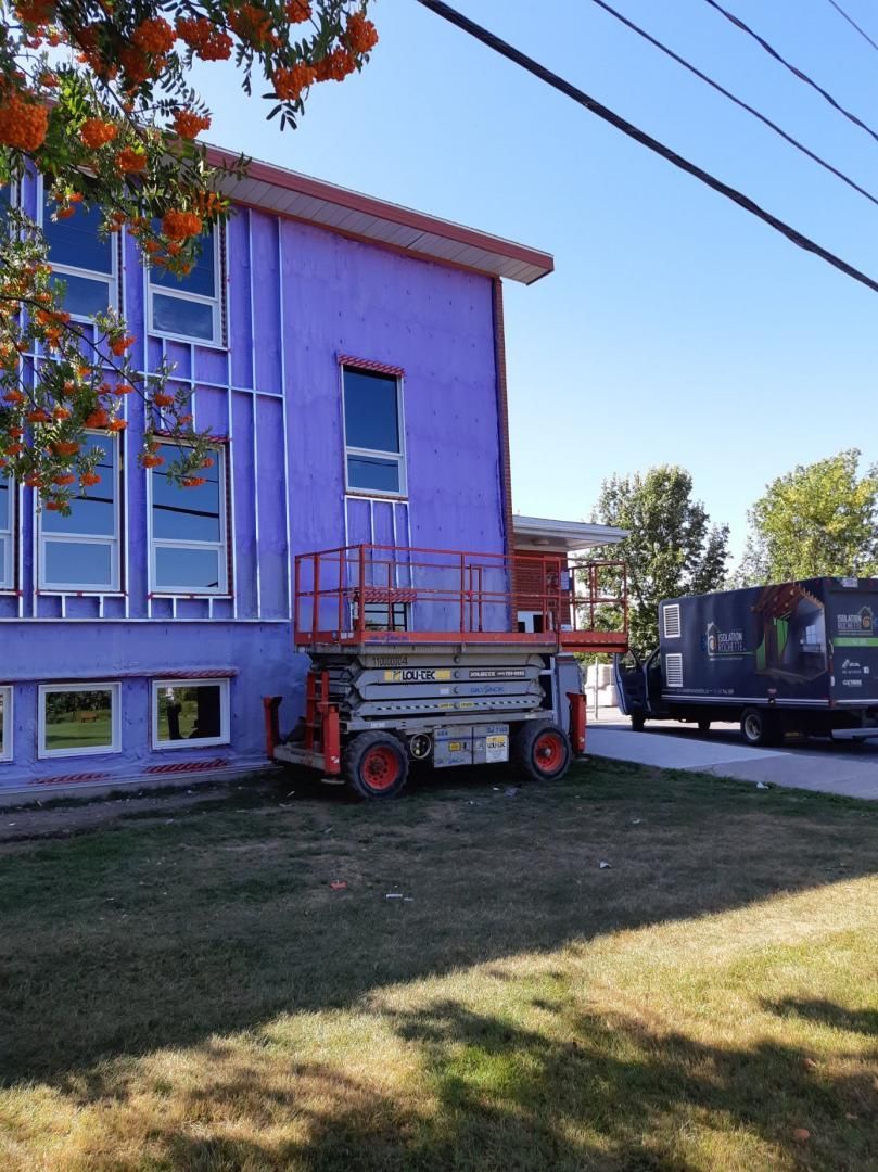 Vue extérieure d'un bâtiment en construction avec plateforme élévatrice. Murs violets, fenêtres et ciel bleu.