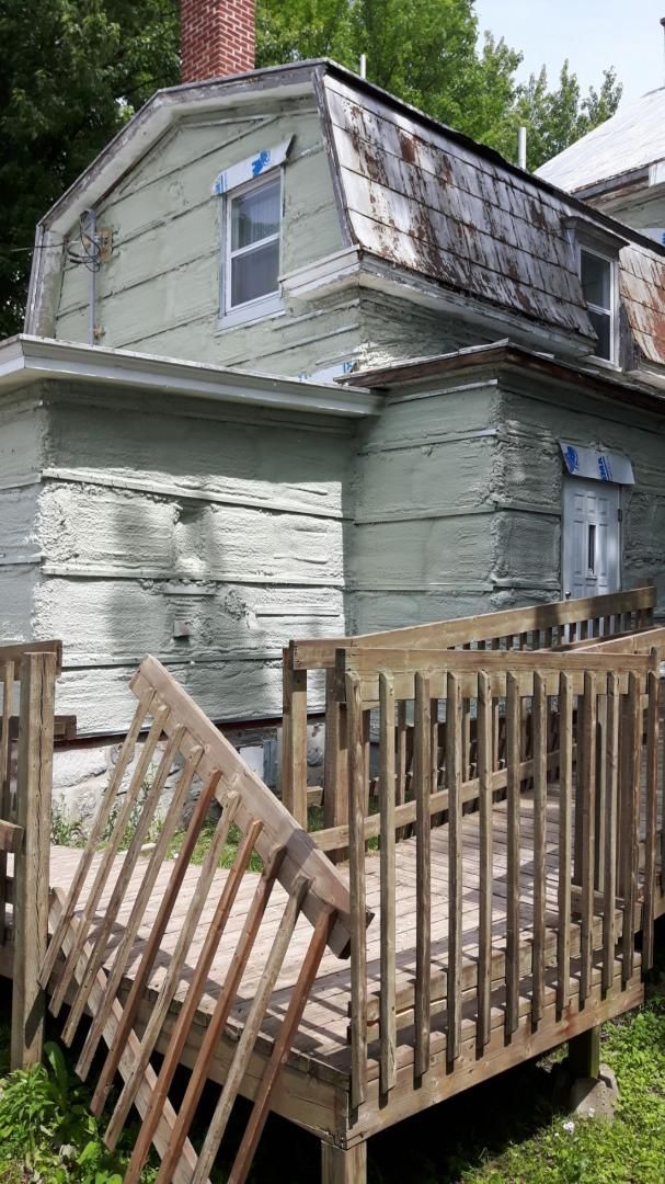 Maison délabrée à deux étages avec terrasse. Revêtement végétalisé, toit couvert de mousse.