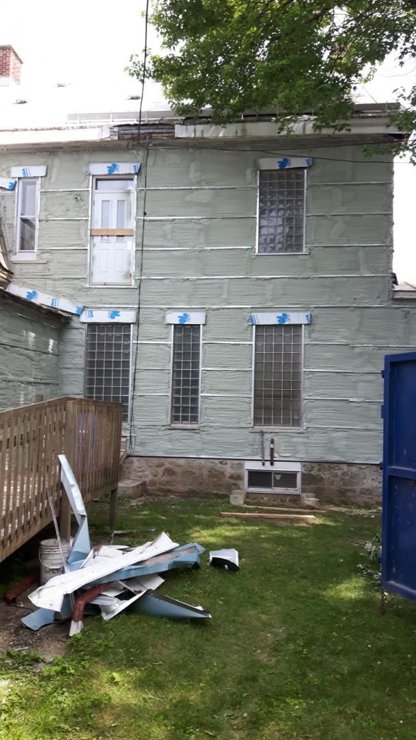 Arrière d'une maison en cours de rénovation avec revêtement vert et débris sur la pelouse.