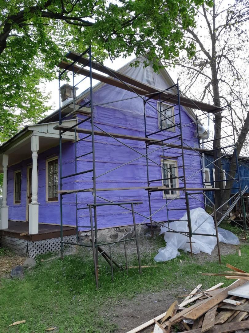 Maison en rénovation, revêtement violet, échafaudage, véranda, cour et matériaux de construction.