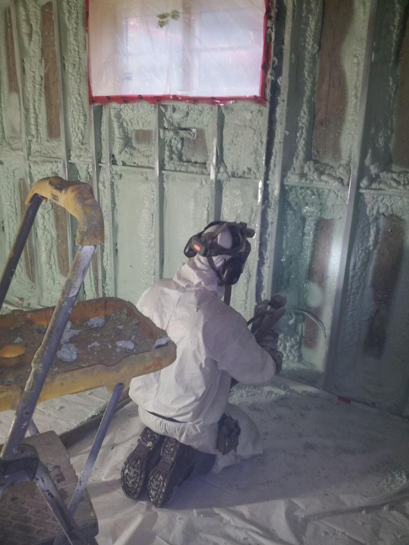 Une personne en combinaison de protection pulvérise de la mousse isolante à l'intérieur d'une structure.