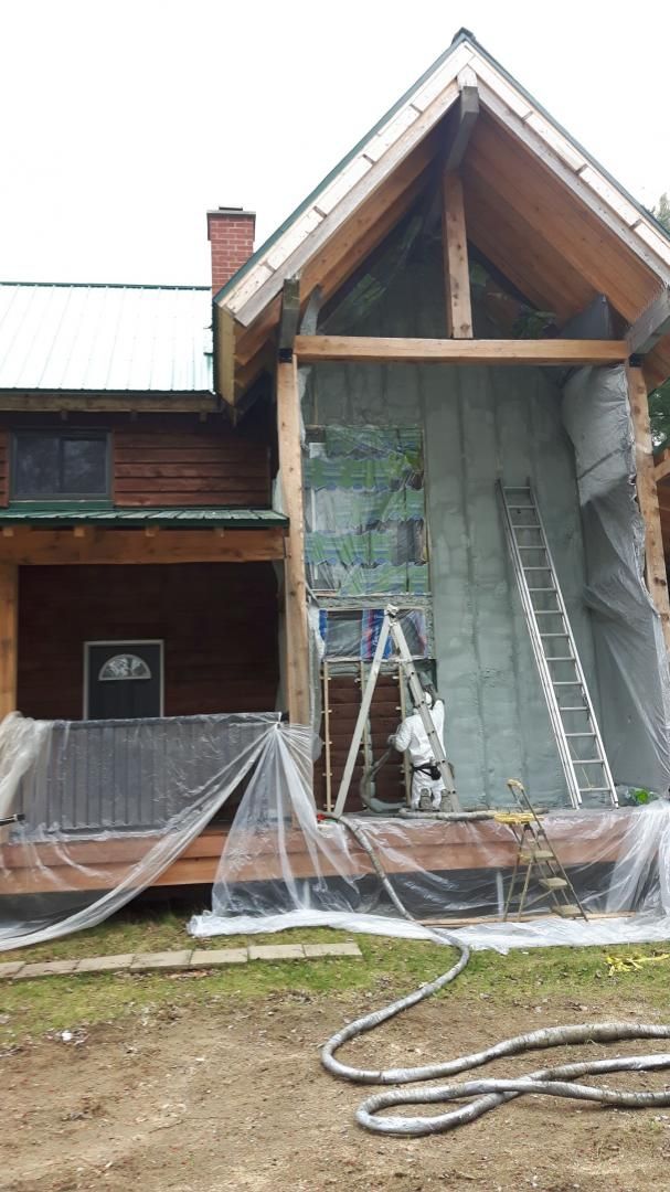 Maison en construction ; isolation en cours d'installation sur le mur extérieur. Échelle et personne en combinaison de protection visibles.