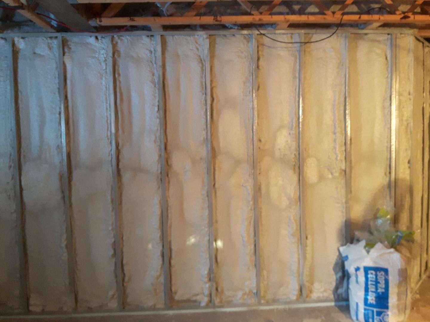 Mur de sous-sol avec isolation en fibre de verre installée entre les montants; un sac d'isolant repose sur le sol.