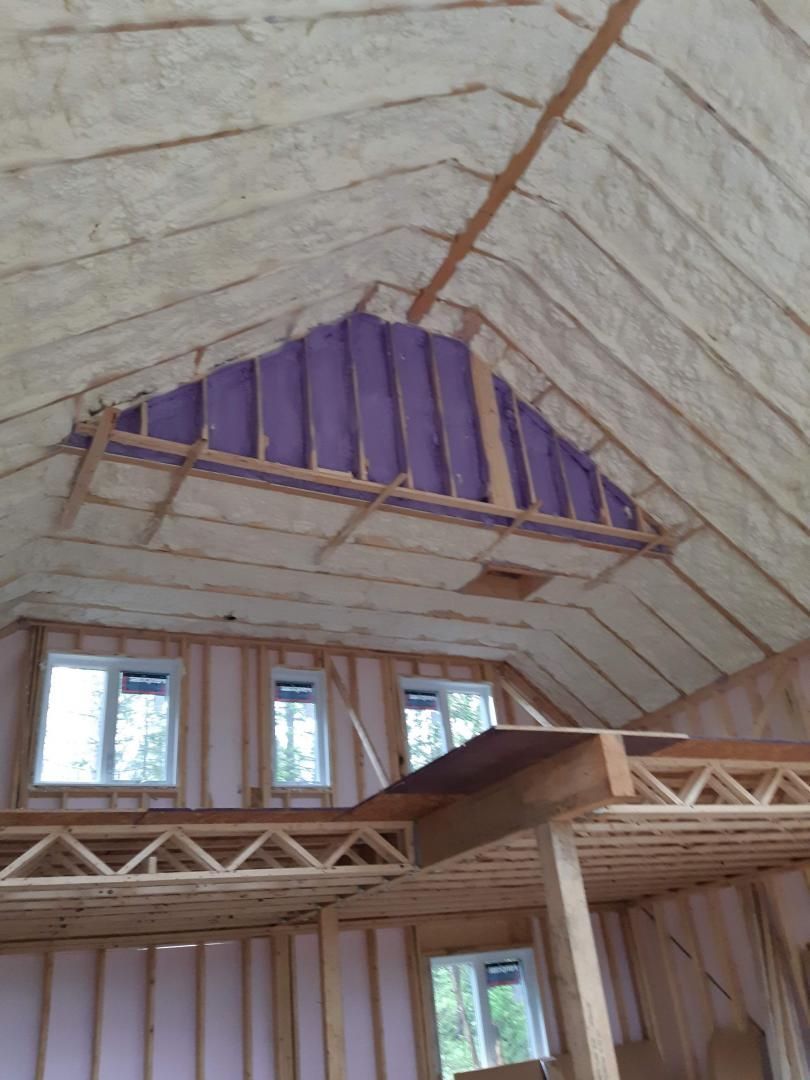 Vue intérieure d'une maison à ossature bois en construction, avec isolation en mousse projetée sur le toit.