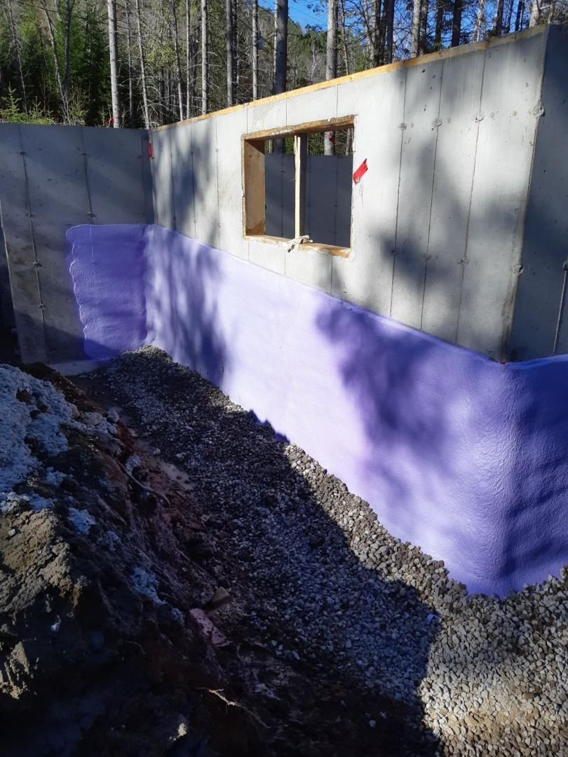 Mur de fondation avec isolation violette, fenêtre et gravier à la base.