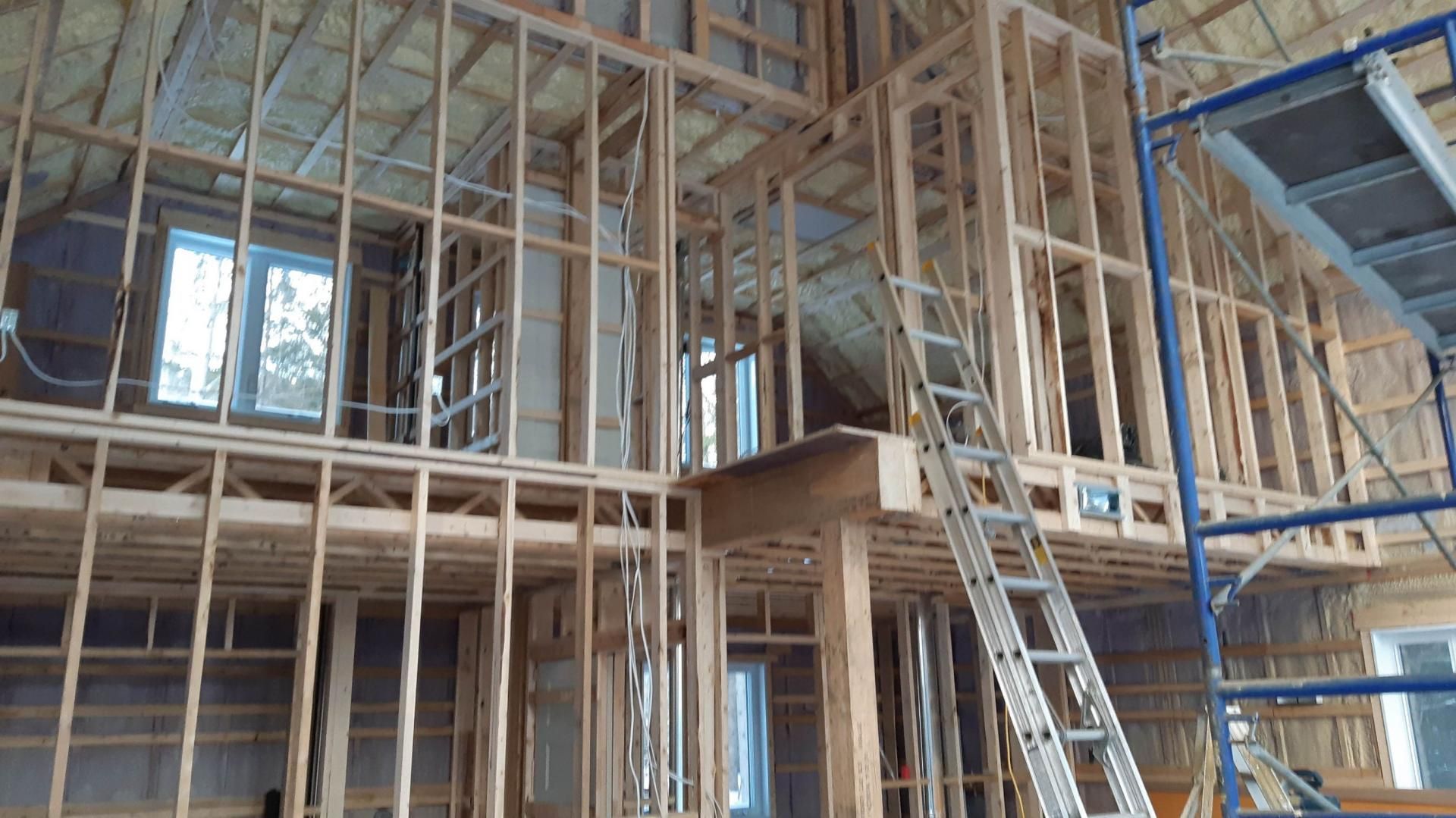Maison à ossature bois en construction, vue intérieure. Montants, fenêtres, échelle.