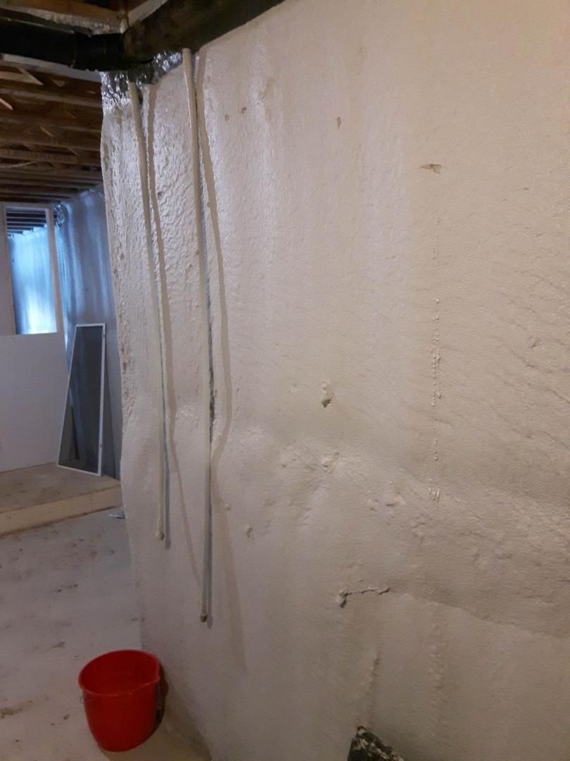 Mur de sous-sol blanc avec tuyaux, seau rouge et poutres de plafond apparentes.