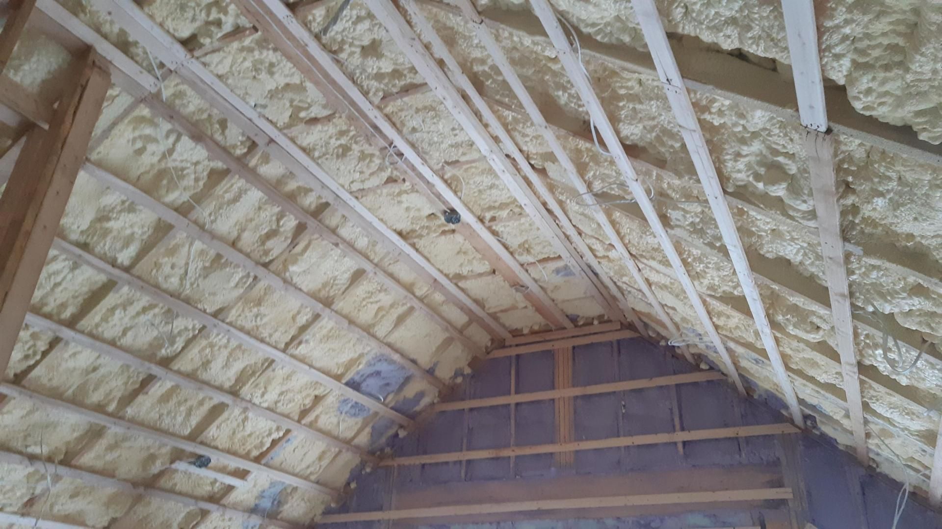 Vue intérieure des combles avec isolation en mousse projetée sur chevrons. Mousse jaune, ossature bois.
