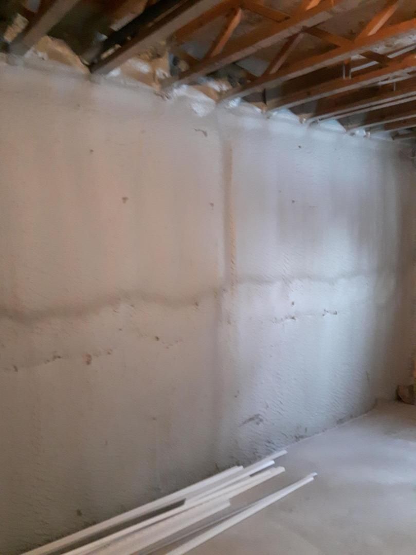 Un mur de sous-sol en béton nu avec des taches d'eau et quelques tuyaux sur le sol.