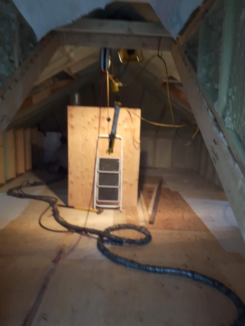 Intérieur mansardé avec structure en contreplaqué, tuyaux et fenêtre. Éclairage tamisé, poutres en bois.