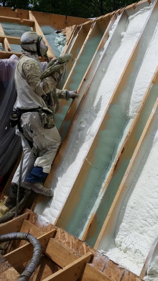 Un ouvrier en équipement de protection pulvérise de la mousse isolante entre les chevrons d'un toit.