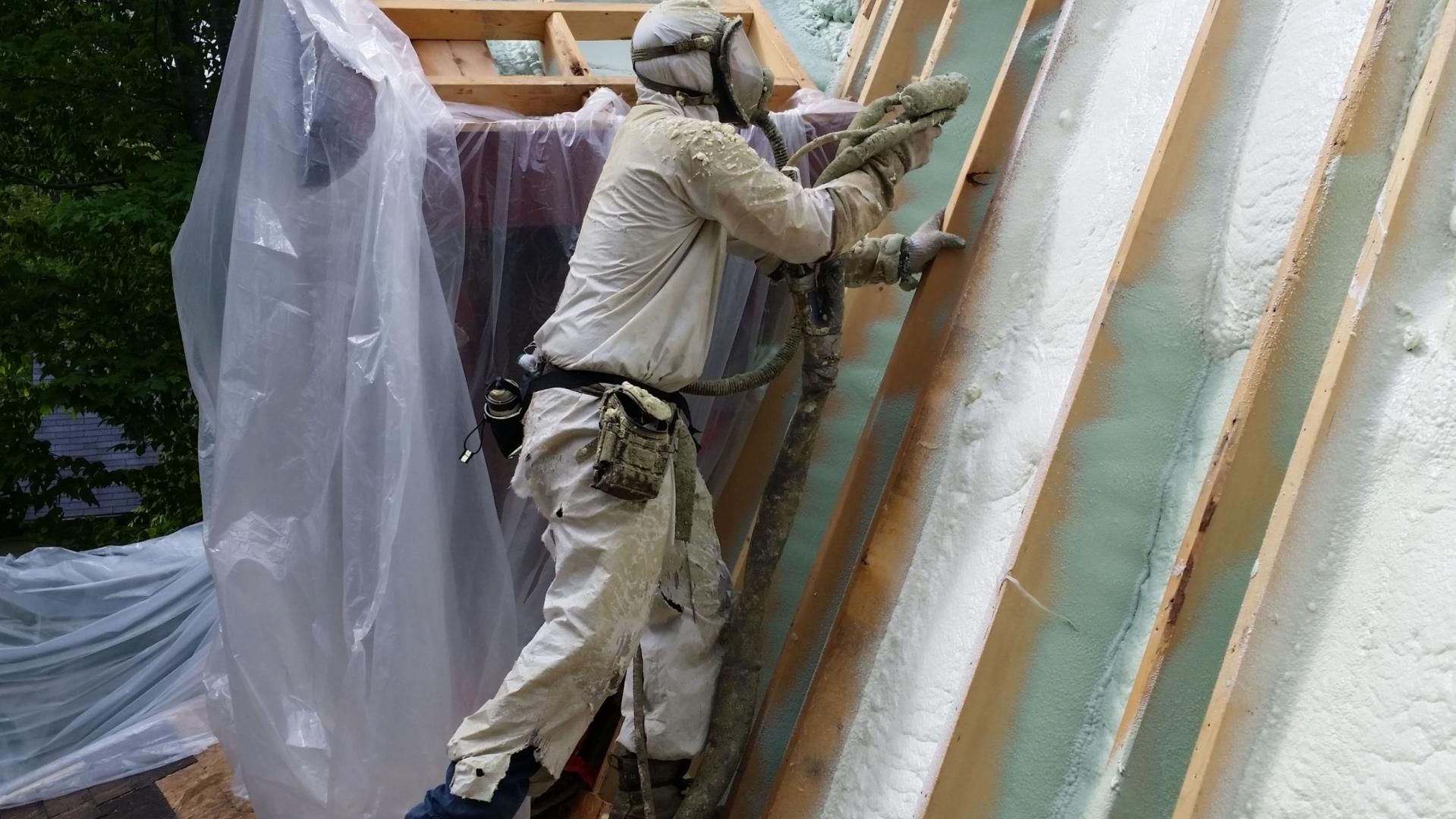 Un ouvrier en équipement de protection pulvérise de la mousse isolante sur les chevrons d'un toit.