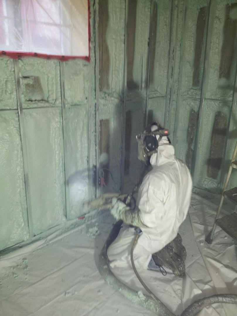 Un ouvrier en équipement de protection pulvérise de la mousse isolante sur un mur.