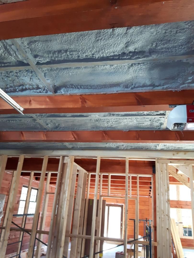 Isolation en mousse pulvérisée sur le plafond du garage, les poutres en bois visibles et les nouveaux montants muraux.