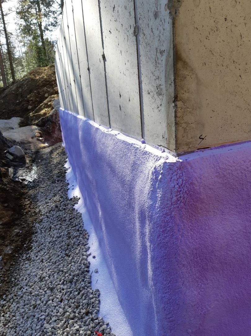 Isolant violet appliqué sur un mur de fondation en béton à côté de gravier, à l'extérieur.