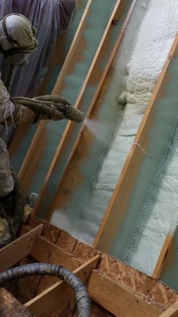 Une personne pulvérise de la mousse isolante expansive entre les chevrons en bois d'un grenier.