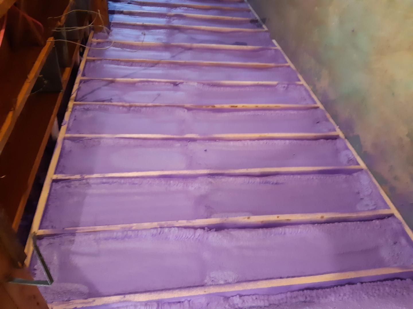 L'isolant violet comble les lacunes dans le cadre d'un escalier en bois, vu d'en haut.